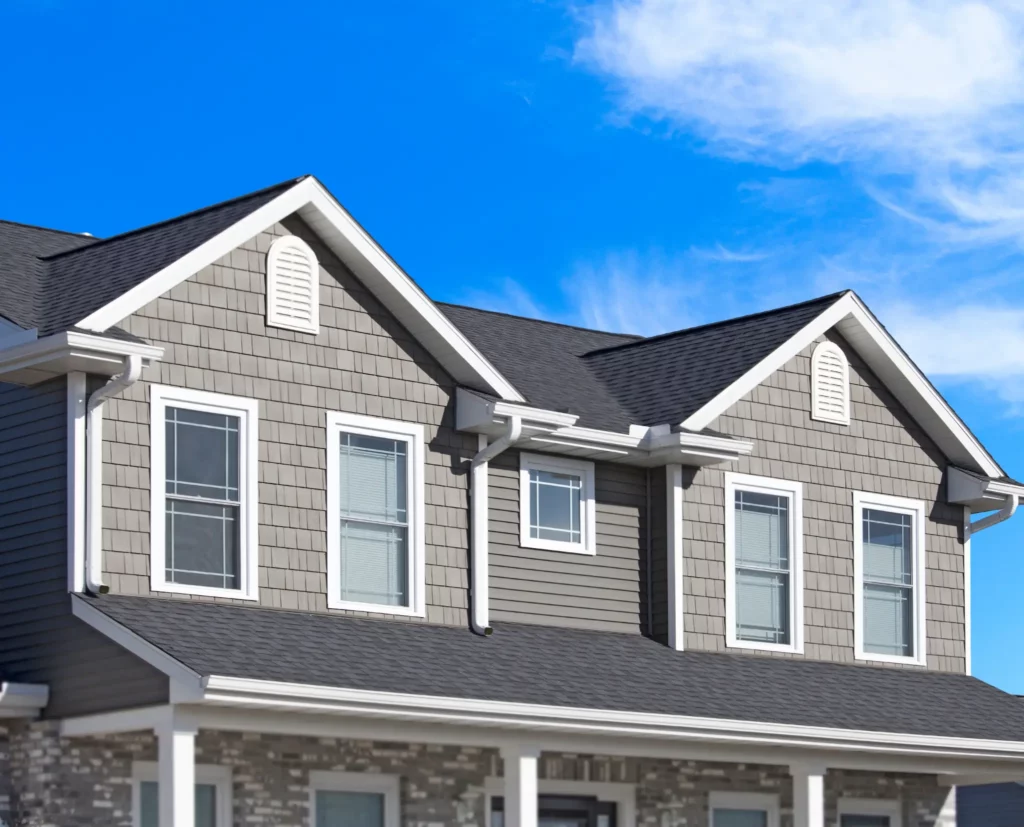 Photo of a house with 2 window peaks, gray siding, and a blue sky with a few clouds.