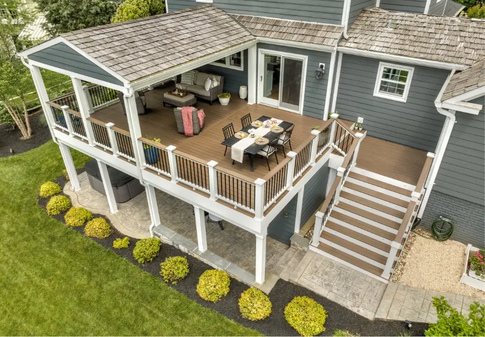 Drone aerial photo of a house with large wrap-around porch that has a partially covered and fully furnished deck on the second floor with stairs.