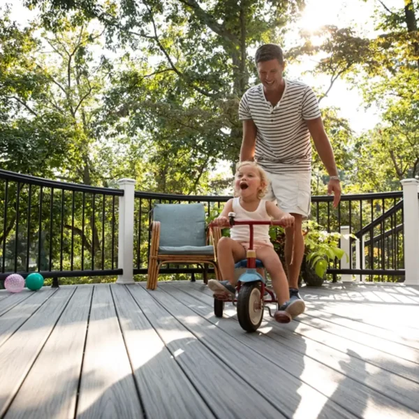 Photo of a proud father encouraging his daughter to ride her tricycle across their Trex deck.