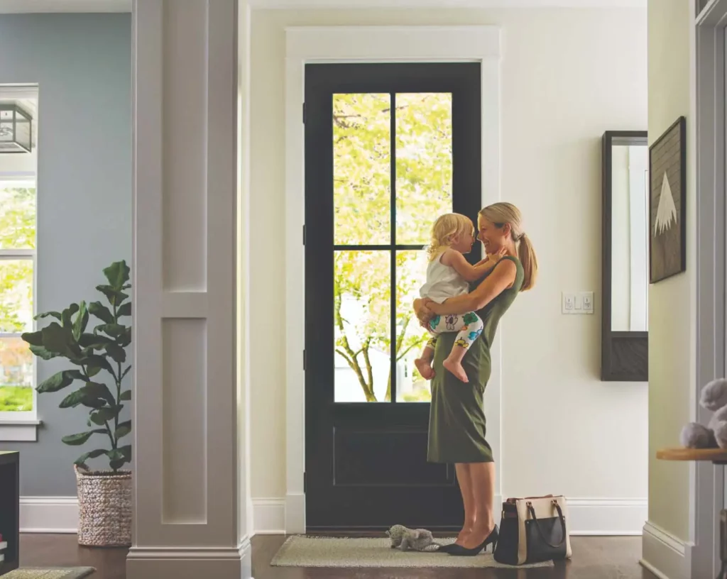 Photo of a mother holding her daughter while they laugh and look in into each other's eyes in front of their door.