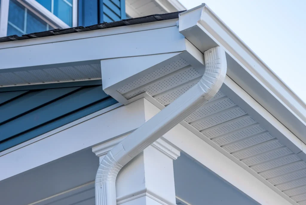 Home with blue siding and white trim and gutters. Close-up of the gutter at the corner of front porch overhang.