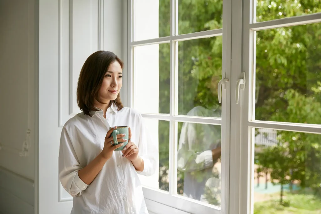 Woman looking out her home window holding a mug.