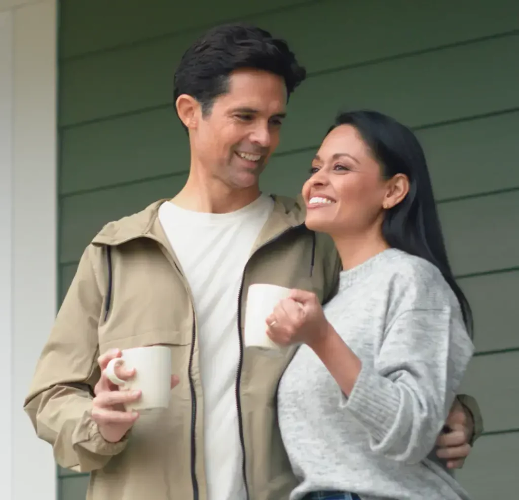 Photo of a couple enjoying cups of coffee on there front porch.