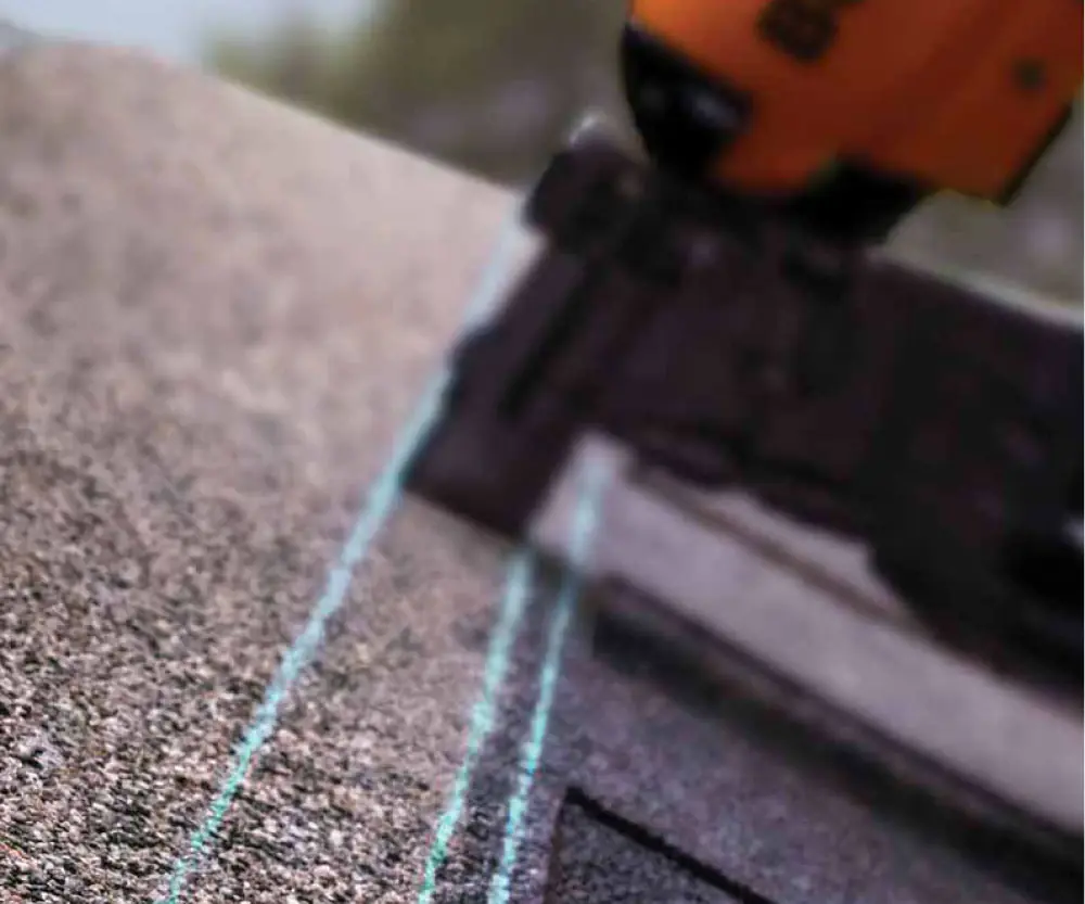 Close-up, blurred photo of a nail gun securing roofing shingles.