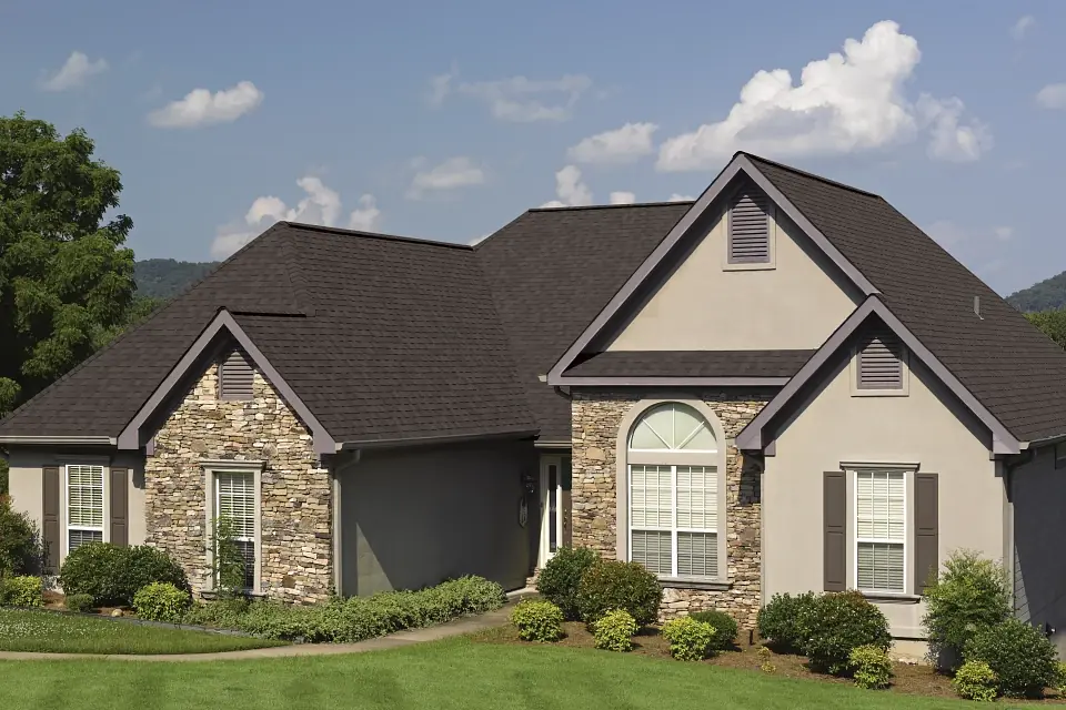 Photo of home with dark shingles and mix of stone and stucco siding.