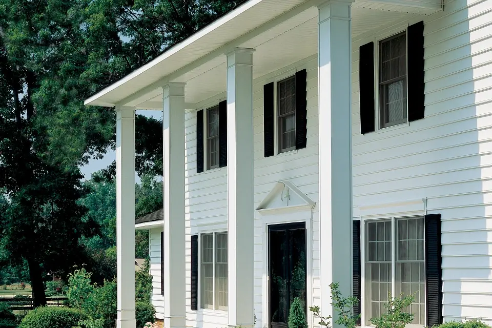 Photo of the front of a home with large decorative pillars holding up the roof for the front patio. White CertainTeed vinyl siding and many windows with black shutters.