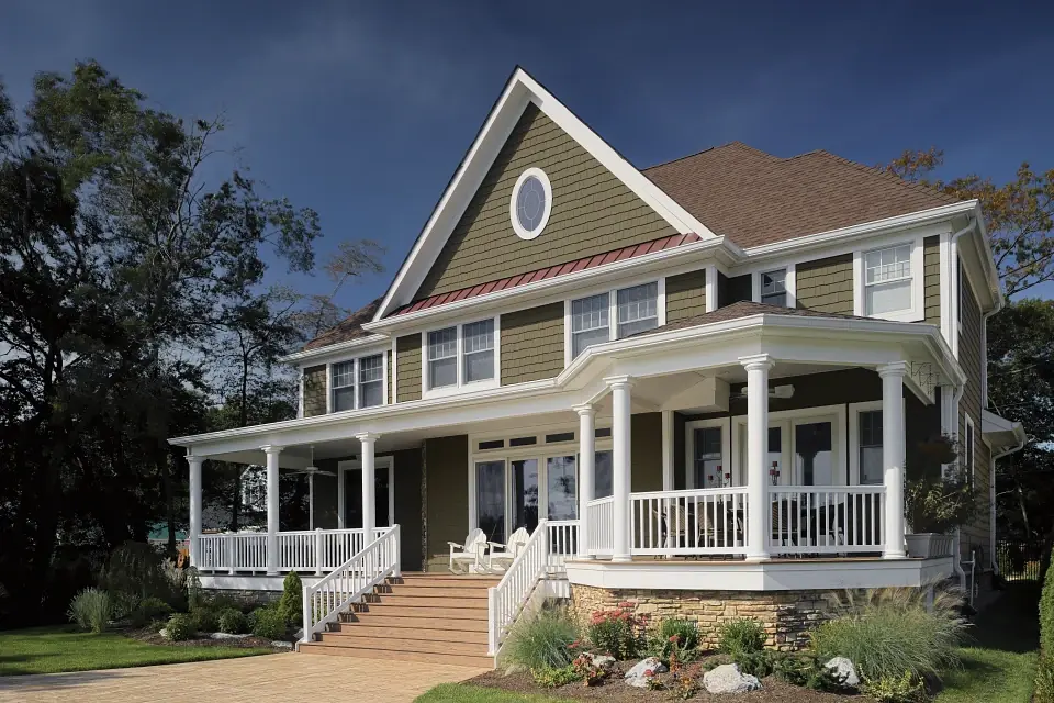 Photo of three-story home with dark tan/brown CertainTeed siding, wrap-around deck and colorful landscaping.