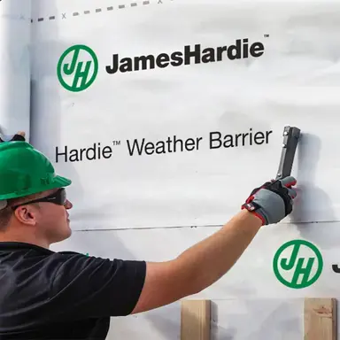 Photo of a team member in green hardhat putting up James Hardie Weather Barrier with logo.