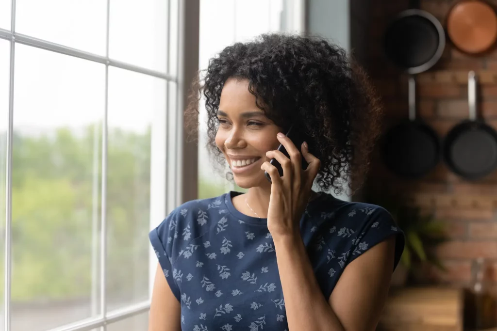 Woman smiling while on her phone and looking out her kitchen window.
