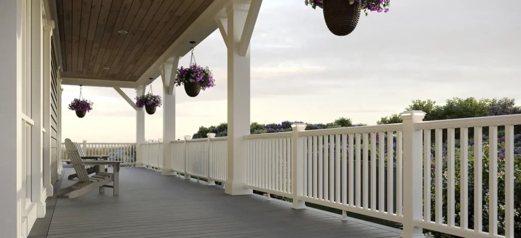 Picture viewing the length of a wrap-around deck with white railing, furnishings, and potted plants hanging from the overhang.