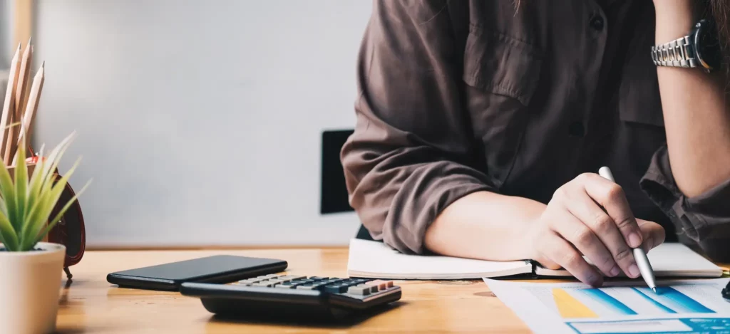 Person sitting at a desk reviewing financial documents with a calculator.