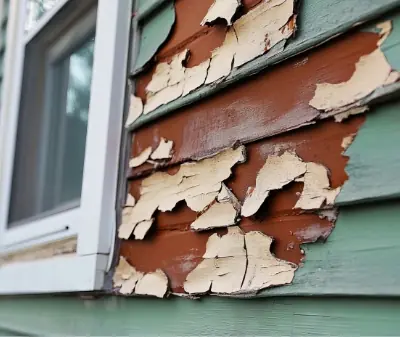 Photo of damaged and fading teal blue-green siding showing a brown color underneath.