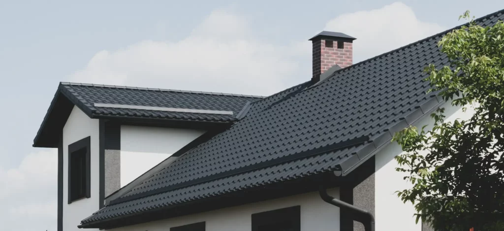 Photo of a home's roof with dormer window, black shingles, and chimney.