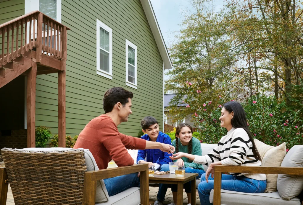 Two-story home with green James Hardie siding and second-story deck. The family is sitting outside at a table.